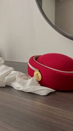 a red hat sitting on top of a wooden floor next to a white cloth covered pillow