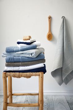 a stack of folded towels sitting on top of a stool next to a wooden spoon