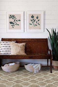 two pictures on the wall above a wooden bench with pillows and baskets underneath it, next to a potted plant