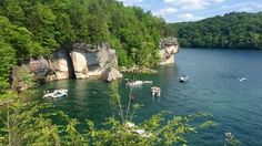 there are many boats that are in the water near some rocks and trees on the shore