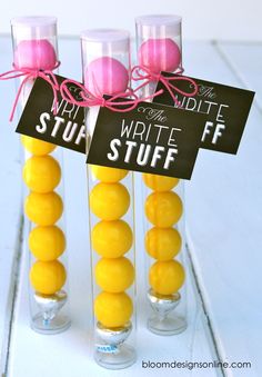 three clear vases filled with yellow and pink candies tied to black signs that read write stuff