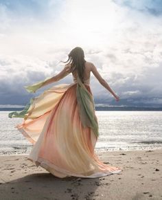 a woman is walking on the beach with her dress blowing in the wind and she's back to the camera