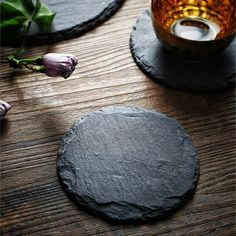 two black slate coasters sitting on top of a wooden table next to a vase