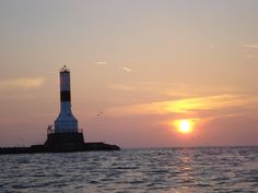 a light house sitting on top of a body of water next to the ocean at sunset