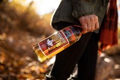 a person is holding a bottle of alcohol in their hand while walking through the woods