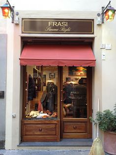 a store front with an open red awning next to it's entrance and potted plant on the sidewalk