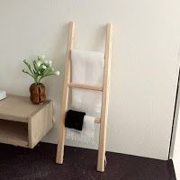 a wooden ladder leaning against a wall next to a vase with flowers and towels on it