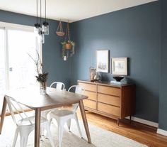 an empty dining room with blue walls and white chairs in the corner, next to a wooden table