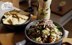 a bowl filled with salad and chips next to a bottle of wine on a table