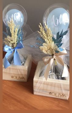 two clear vases with blue and white flowers in them on top of a wooden table