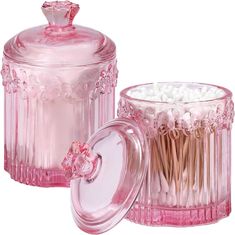 two pink glass containers with toothpicks in them and one container filled with cotton swabs