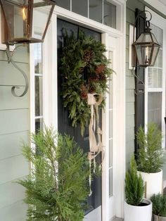 two potted plants are on the front porch and one is holding a wreath with pine cones