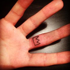 a person's hand with a small crown tattoo on the middle of their finger