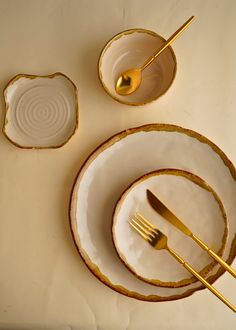 an empty plate with two gold forks and one silver spoon on it, next to another set of dishes