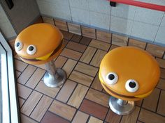 two yellow stools with googly eyes are on the tiled floor next to each other