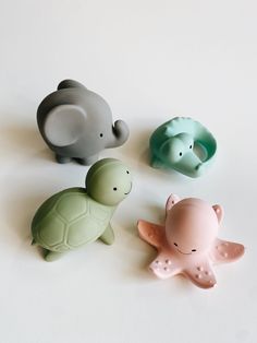 three small plastic animals sitting next to each other on a white surface with one elephant and the other turtle