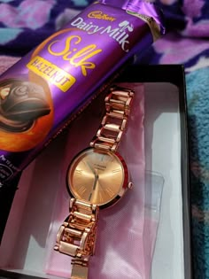 a watch and caddie's milk chocolate are sitting in a gift box on a bed