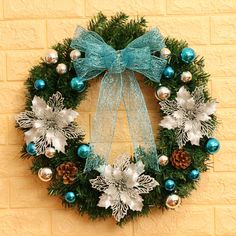 a christmas wreath with blue and silver ornaments hanging on a brick wall next to a green bow