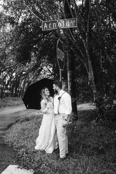 a man and woman standing next to each other under an umbrella near a stop sign