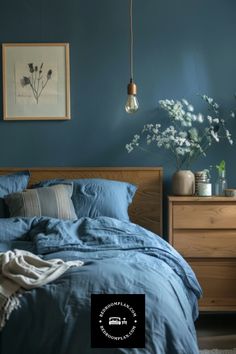 a bed with blue sheets and pillows in a bedroom next to a wooden chest of drawers