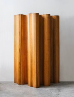 three tall wooden columns sitting next to each other on a cement floor in front of a white wall