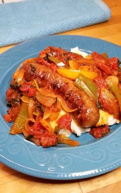 a blue plate topped with meat covered in peppers and onions on top of a wooden table