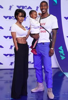 a man holding a baby standing next to two women in front of a blue wall