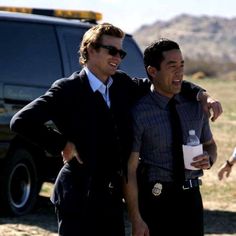 two men standing next to each other in front of a vehicle and one holding a bottle