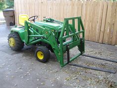 a green tractor parked next to a wooden fence