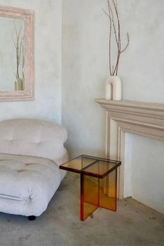 a living room with a white couch, mirror and table in front of the fireplace