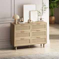 a wooden dresser sitting next to a wall with pictures on it and plants in the corner