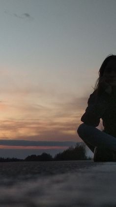 a woman sitting on top of a surfboard next to the ocean at sunset or dawn