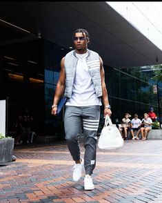 a man walking down the street carrying a white bag and wearing grey sweatpants with his hands in his pockets