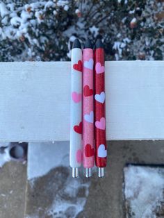 two pens with hearts on them sitting next to each other in front of snow covered ground