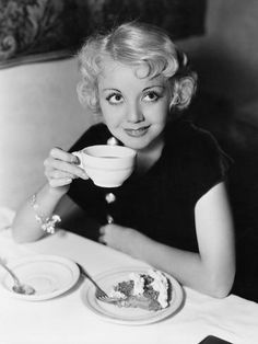 a black and white photo of a woman drinking from a cup with cake on it