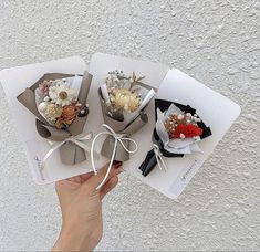 three small flower bouquets tied together with white string on top of each other and held in someone's hand