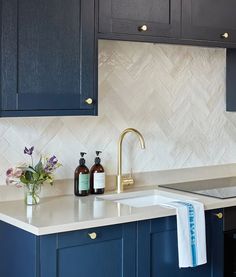 a kitchen with blue cabinets and white marble counter tops, gold faucet, soap dispenser