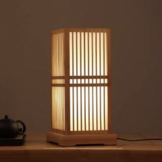 a table lamp sitting on top of a wooden table next to a teapot and cup