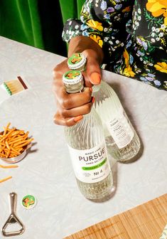 a woman is holding two bottles of puree on a table with other items around her