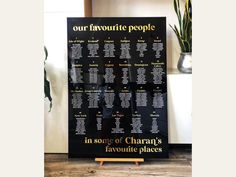 a black and gold wedding seating chart on a wooden stand with potted plants in the background