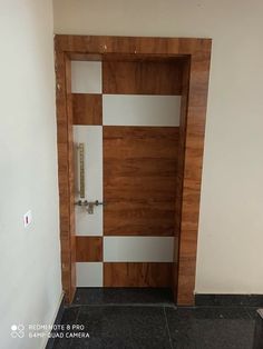 an empty room with a wooden door and tile flooring on the ground, in front of a white wall