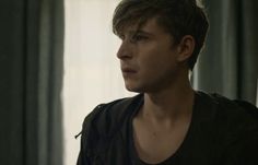 a young man standing in front of a window wearing a black shirt and dark vest