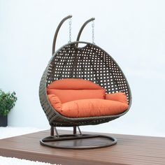 a hanging chair with an orange pillow on it's back and some plants in the background