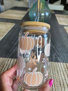 a person holding up a glass jar with pumpkins and stars painted on the side