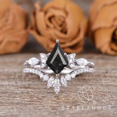 a black diamond ring sitting on top of a wooden table next to some rose petals