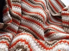 an orange and white crocheted blanket laying on top of a bed next to a pillow