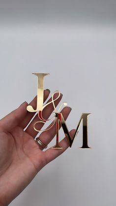 a person's hand holding three different types of metal letters that spell out the letter m