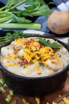 a black bowl filled with potato soup on top of a wooden cutting board next to vegetables