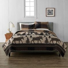 a bed in a room with wooden floors and white walls, has a moose quilt on it