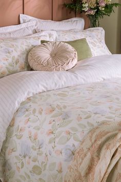 a bed with white and pink comforter, pillows and flowers on the headboard